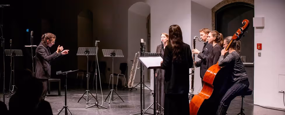 A small ensemble of 5 musicians and a conductor in concert