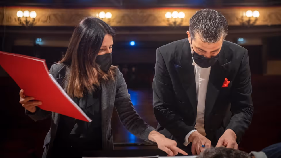 Two people dressed in black discuss a score wearing face masks